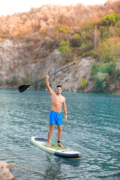Jongeman met paddle board voor sup surfen in de rivier - Foto, afbeelding