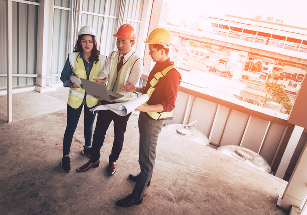 Tres ingenieros masculinos y femeninos están discutiendo en documentos y computadoras en un sitio de construcción de edificios. - Foto, Imagen