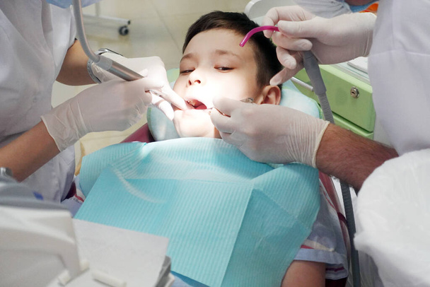 Dentysta badający usta chłopca. Młody chłopiec wygląda odważnie w gabinecie dentystycznym - Zdjęcie, obraz