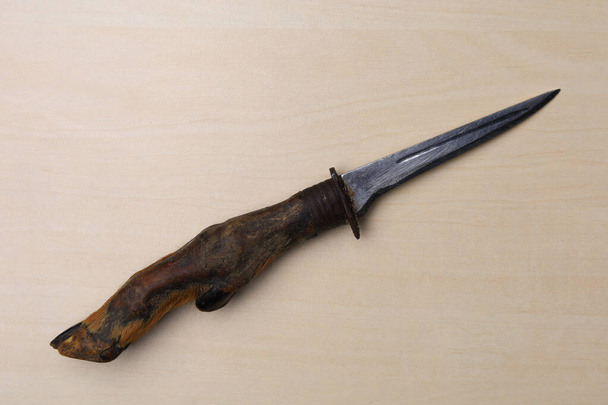 Starý lovecký nůž vyrobený z kozího kopyta v souladu se všemi pravidly broušených zbraní leží na dřevěném stole. - Fotografie, Obrázek