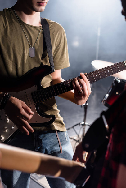 KYIV, UKRAINE - AUGUST 25, 2020: Cropped view of rock band musician playing bass guitar with pick with blurred guitarist on foreground - Photo, image