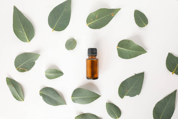 A top view of a bottle of amber essential oil surrounded by eucalyptus gum leaves on the table - Zdjęcie, obraz