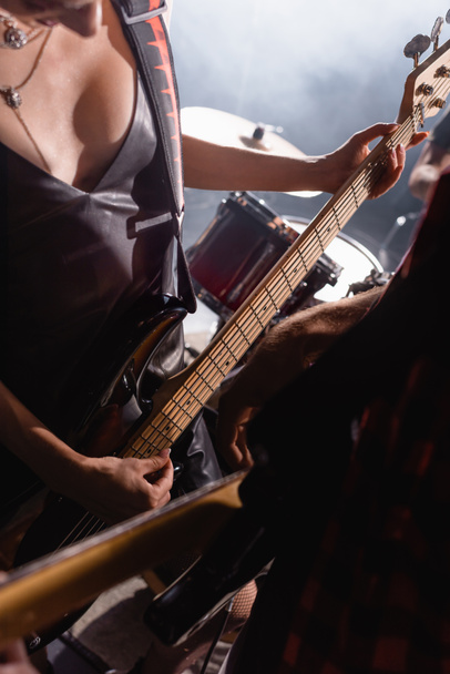 KYIV, UKRAINE - AUGUST 25, 2020: Woman touching guitar strings standing near drums with blurred guitarist on foreground - Foto, afbeelding