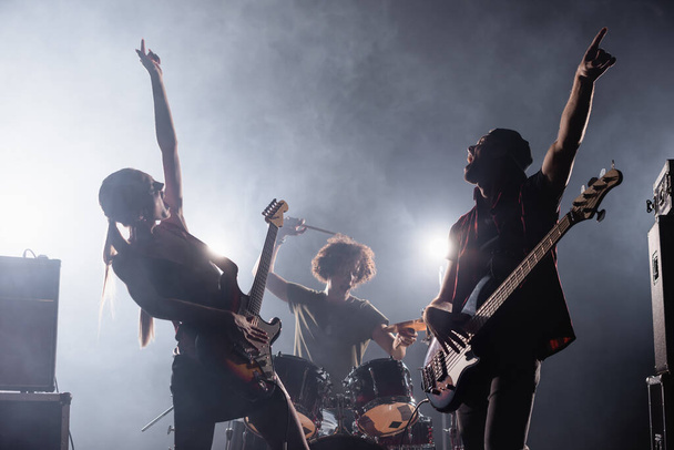 KYIV, UCRANIA - 25 de agosto de 2020: guitarristas de la banda de rock con las manos en el aire cantando con humo y batería en el fondo - Foto, Imagen