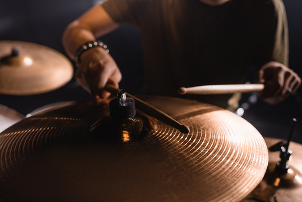 Gekropte weergave van metalen cimbalen met wazig muzikant met drumstokken op achtergrond - Foto, afbeelding
