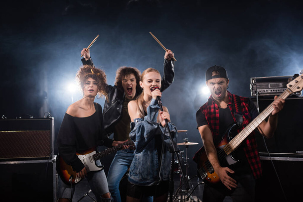 KYIV, UKRAINE - AUGUST 25, 2020: Rock band musicians yelling while holding musical instruments with backlit on black - Foto, imagen