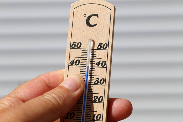 A closeup of a person holding a wooden wall thermometer under the sunlight with a blurry background - Foto, Imagen