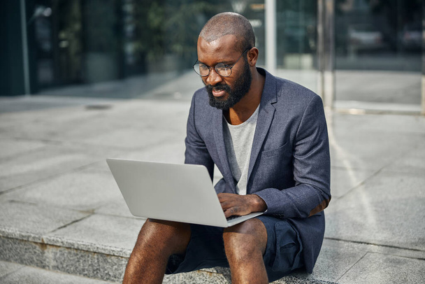Attentive dark-skinned man looking at screen of laptop - Photo, image