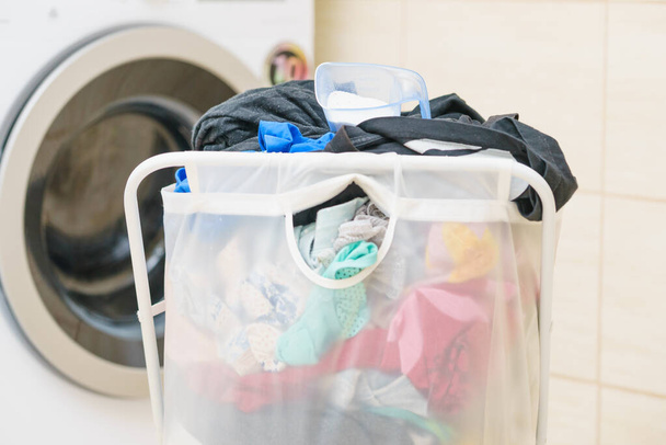Transparent white big standing laundry basket full of colorful dirty clothes. Bathroom utensils concept. - Foto, Bild