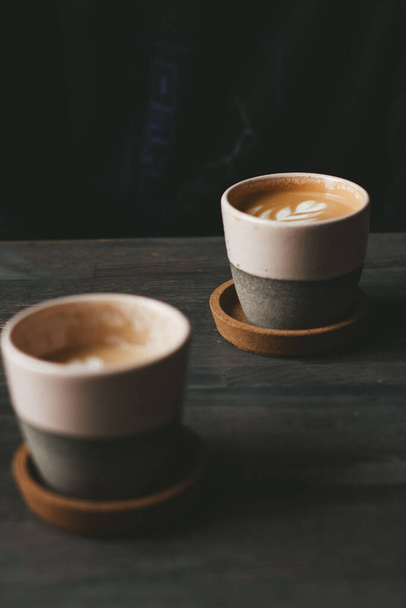 A vertical shot of two ceramic cups of foamy caffe latte on a wooden table - Photo, Image