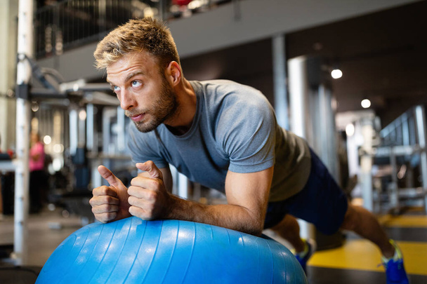 Happy fit man doing fitness exercise on pilates ball in gym - Foto, imagen