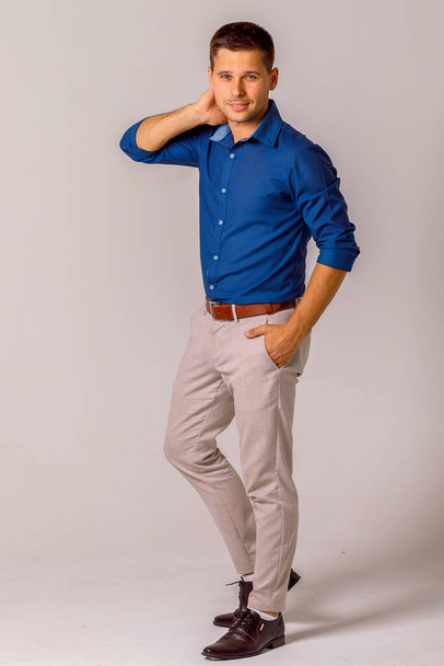 Young man dressed in classic style, blue shirt and white pants on a white background - Foto, imagen