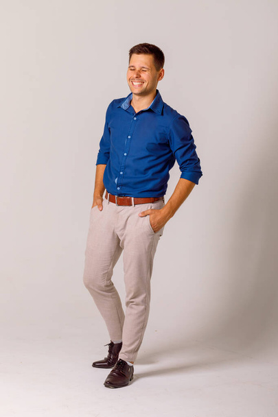 Молодой человек, одетый в классический стиль, синяя рубашка и белые брюки на белом фоне - Фото, изображение