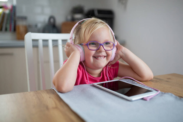 Szczęśliwy maluch dziewczyna słucha muzyki na różowe słuchawki w domu. - Zdjęcie, obraz