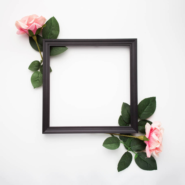 A top view of a black square frame surrounded by roses isolated on a white background - Fotoğraf, Görsel