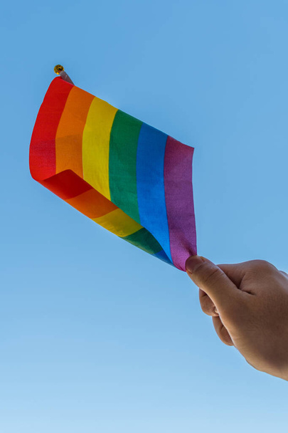 Низький кут пострілу чоловіка, який тримає прапор гордості ЛГБТ з синім фоном неба. - Фото, зображення