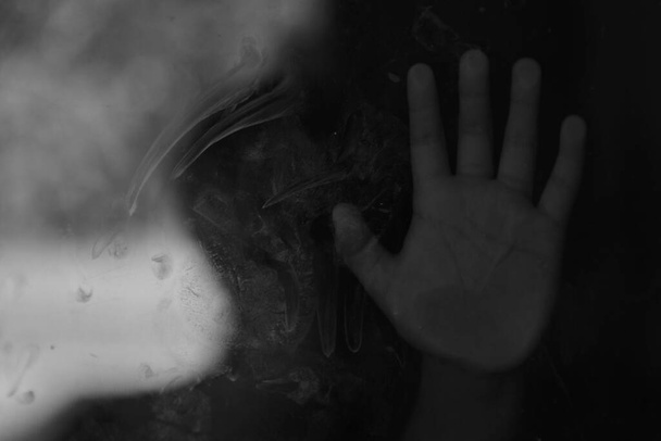 Un monochrome de la main d'un enfant contre une fenêtre en verre - - abus, concept de dépression - Photo, image