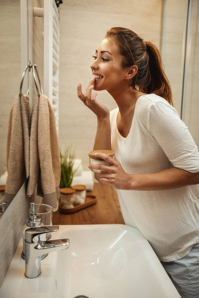 Aufnahme einer attraktiven jungen Frau, die im heimischen Badezimmer Feuchtigkeitscreme für das Gesicht aufträgt. - Foto, Bild