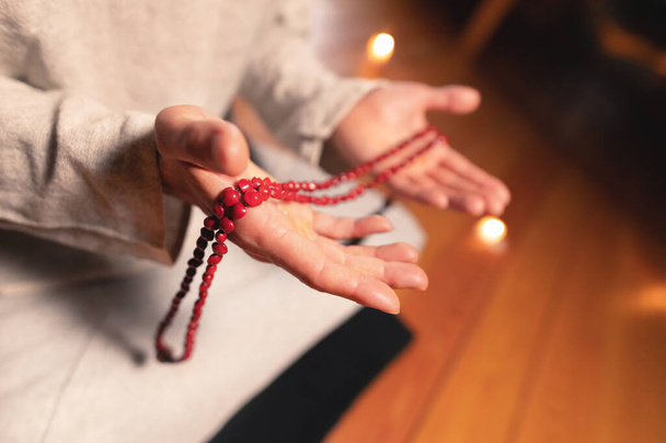 Close-up of a male monks hand holding a red wooden rosary in a dark study room. Religion faith - Φωτογραφία, εικόνα