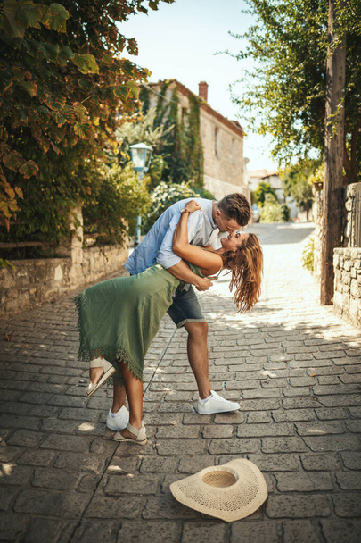Ένα όμορφο νεαρό ζευγάρι διασκεδάζει και χορεύει στο δρόμο περπατώντας κατά μήκος μιας μεσογειακής πόλης. Απολαμβάνονται το καλοκαίρι ηλιόλουστη μέρα. - Φωτογραφία, εικόνα