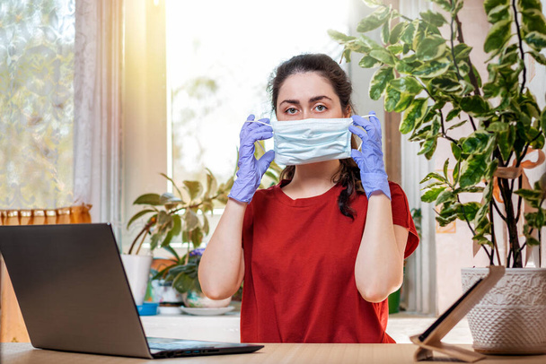Freelance.Una giovane donna caucasica in guanti, indossando una maschera medica.Home office, laptop sul tavolo.Concetto di quarantena, auto-isolamento e coronovirus. - Foto, immagini