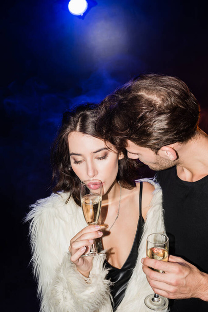 Man in shirt looking at seductive brunette woman with glass of champagne with backlit on black - Fotografie, Obrázek