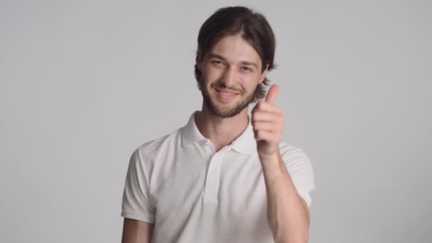 Atrakcyjny, stylowy facet z pewnością pokazujący ci gest i kciuk przed kamerą na białym tle. Jak ekspresja - Materiał filmowy, wideo