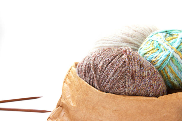 Des boules de fils de couleurs nues dans un sac artisanal et des aiguilles à tricoter sur un fond lumineux. Artisanat sur fond blanc avec espace de copie. Le tricot comme concept de passe-temps féminin - Photo, image