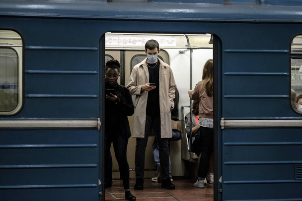 Moscow. Russia. September 25, 2020 A man in a subway car is looking at his smartphone with enthusiasm. The passenger has a protective medical mask on the face. Second wave of coronavirus. - Photo, Image