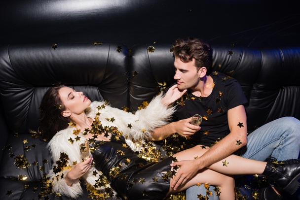 Verleidelijke vrouw aanraken vriendje kin kijken naar elkaar, terwijl confetti vallen in nachtclub - Foto, afbeelding