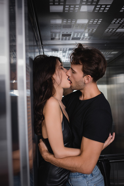 Siyah elbiseli tutkulu bir çift asansörde sarılıp öpüşüyor. - Fotoğraf, Görsel