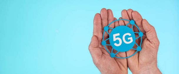 Manos sosteniendo un letrero 5G sobre fondo azul claro; Concepto de 5G - Foto, imagen