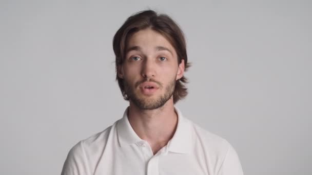 Jonge aantrekkelijke bebaarde man met zelfverzekerd stiltegebaar op camera over grijze achtergrond. Shh uitdrukking - Video