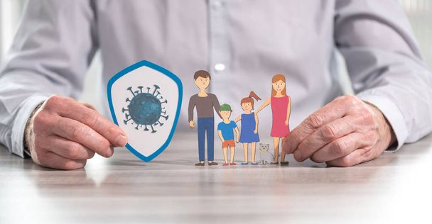 Elinde virüs ve aile olan bir kalkan tutan adam; covid-19 salgını sırasında aile sigortası kavramı - Fotoğraf, Görsel