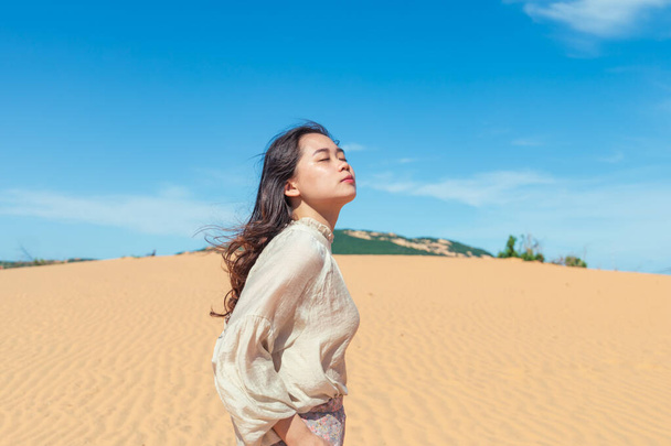 An attractive young Asian female with beautiful long hair walking in a desert area and enjoying the nice weather under a cloudy sky - Foto, Imagem