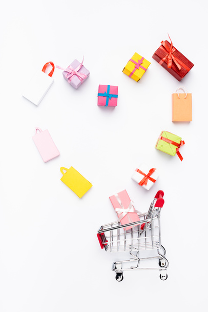 Top view of heart from toy shopping bags and gifts near cart on white background - 写真・画像
