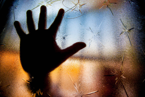 Silhouette of human hand against window glass with color background - Photo, Image