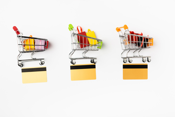 Top view of credit cards near shopping carts with toy gifts and bags on white background - Foto, Imagen