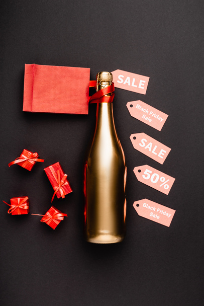 Bovenaanzicht van gouden fles champagne in de buurt van prijskaartjes en speelgoed geschenken op zwarte achtergrond  - Foto, afbeelding