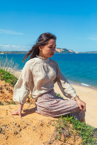 An attractive young Asian female with beautiful long hair sitting on a beach and enjoying the nice weather - Zdjęcie, obraz
