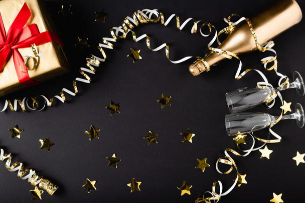 Vue du dessus de la bouteille de champagne et des verres près de la boîte cadeau et du décor sur fond noir  - Photo, image