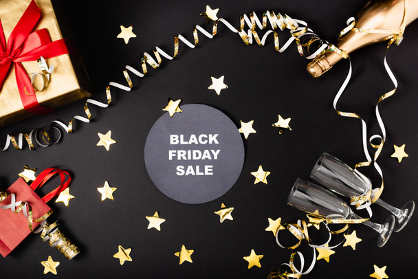Top view of round with black friday sale lettering near festive decor, bottle of champagne and gift on black background  - Photo, Image
