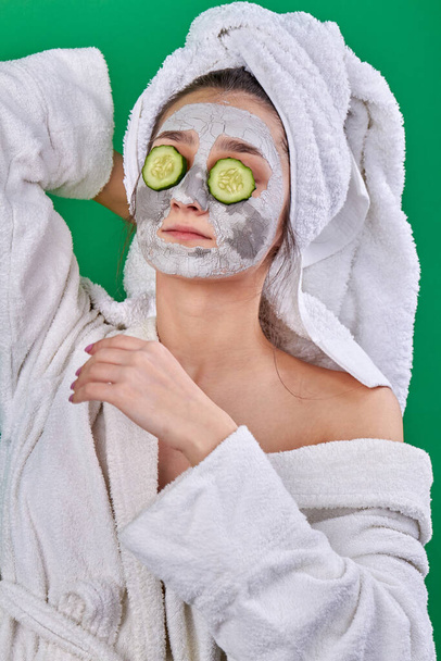 Portrait of girl with facial clay mask and cucumber slices. - Фото, изображение