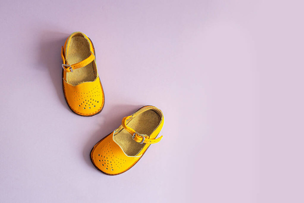 Sapatos de bebê amarelo brilhante em fundo lilás com copyspace. Conceito de roupa de bebé. Vista superior, flat lay - Foto, Imagem