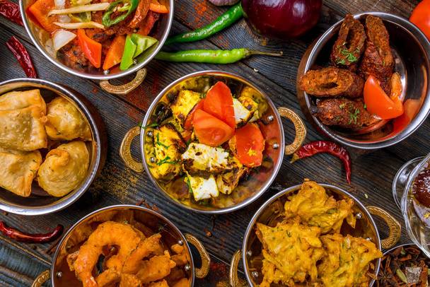 Assorted indian food set on wooden background. Dishes and appetisers of indeed cuisine, rice, lentils, paneer, samosa, spices, masala. Bowls and plates with indian food - Fotografie, Obrázek