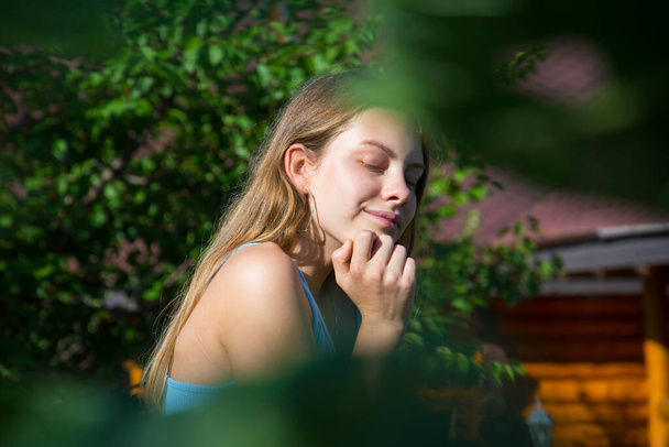 In de zomer, op een zonnige dag, staat er een mooi meisje in het dorp vlakbij een huis met zonnebloemen.. - Foto, afbeelding