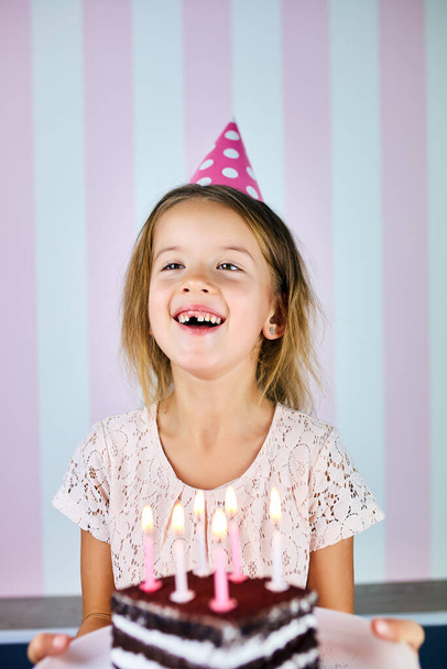 Little blonde girl smiling in birthday pink cap, a chocolate birthday cake with candles. Child celebrates her birthday. Happy birthday. - Photo, Image