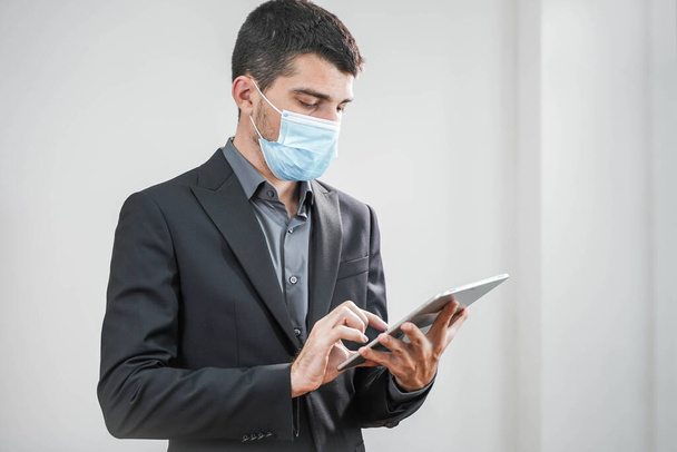 Coronavirus. Business man wearing protective mask in a white background. Business man with face masks back to work in office after lockdown. Small company concept. Working with tablet. - Fotoğraf, Görsel