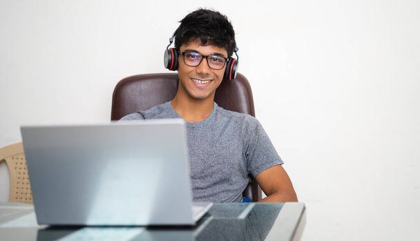 Adolescente indio que trabaja con el ordenador portátil mientras escucha música en la oficina. - Foto, Imagen