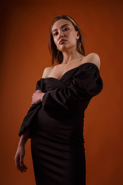 elegante modelo con vestido negro con escote profundo posando sobre fondo naranja - Foto, imagen